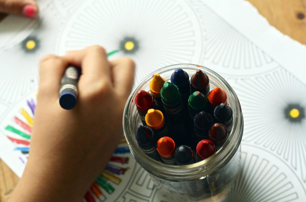 A child drawing with colorful crayons, fostering creativity and fun in a learning environment.